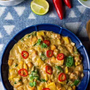 Blue bowl full of peanut colored stew with butternut squash, spinach leaves, and peanuts