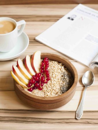 Bowl of Vegan Apple Cinnamon Oatmeal made on stove top - topped with apple slices, red currant, chia seeds and puffed quinoa