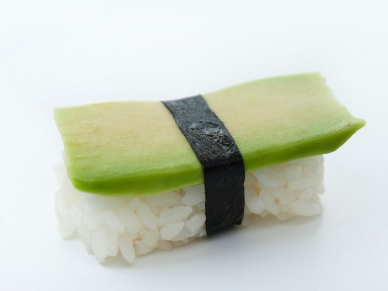 One nigiri with rice at the bottom and avocado slice on top wrapped with a thin seaweed sheet band