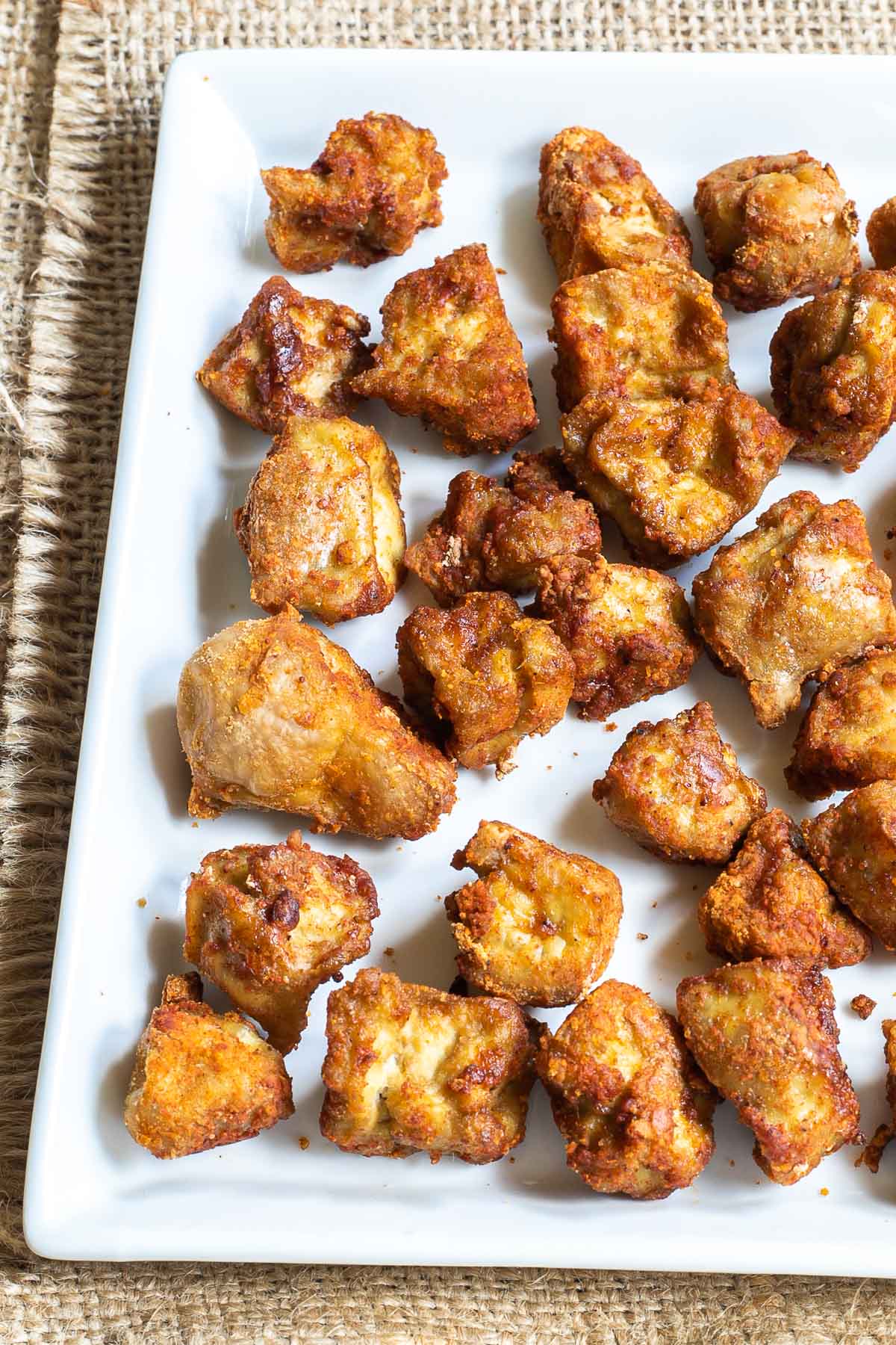 Baked, redish brown tofu pieces on white square plate.
