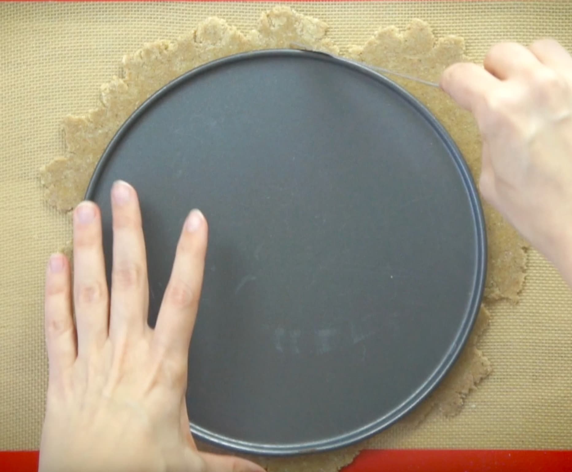 A hand is holding a round cake pan bottom and cutting a rolled out dough around it.