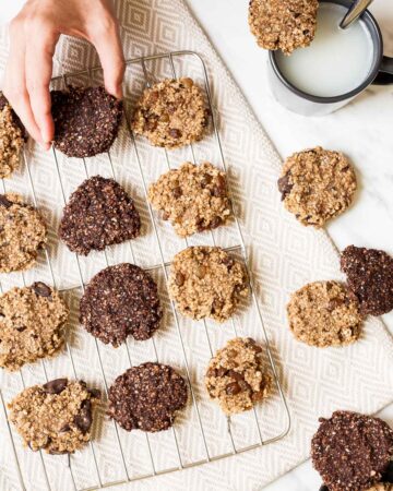 Light and dark brown oatmeal cookies on a wire rack. A hand is taking one.