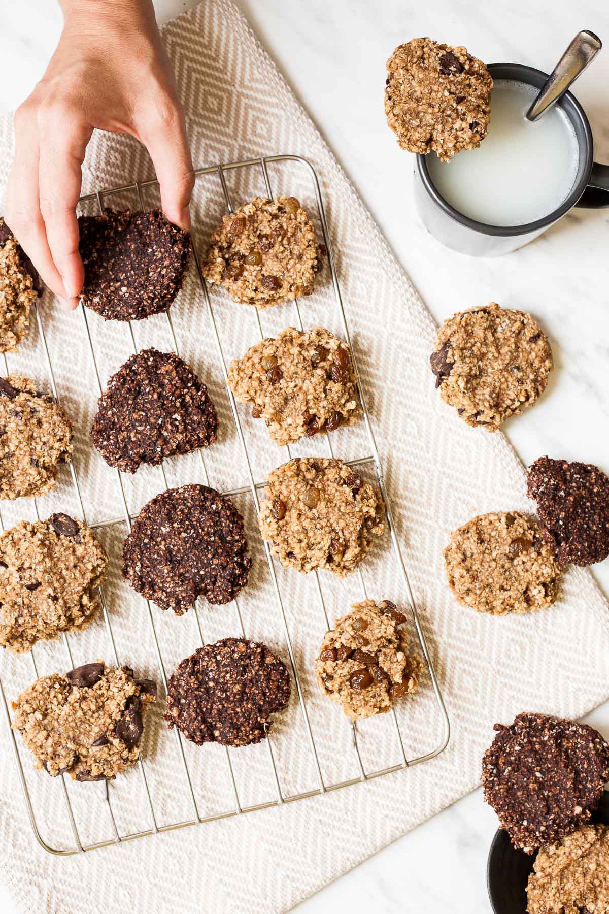 Light and dark brown oatmeal cookies on a wire rack. A hand is taking one.