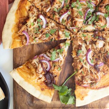 Sliced pizza with thin shredded chicken like threads, red onion slices, orange sauce and fresh chopped herbs