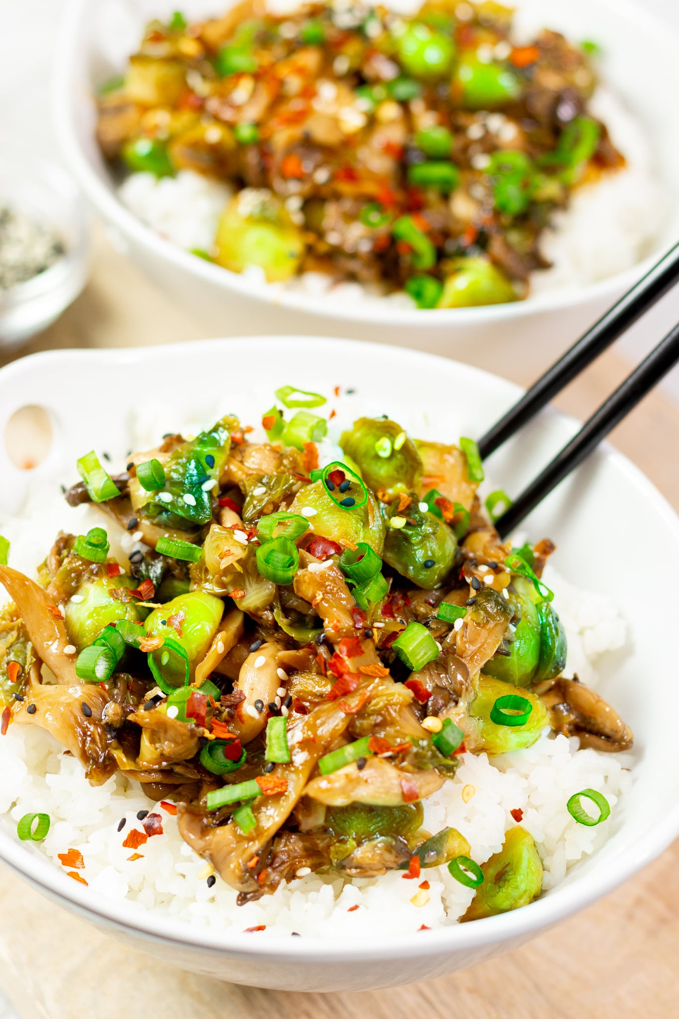 White bowl with brown mushroom shreds, Brussels sprouts, white sesame, green spring onion slices on top of rice.