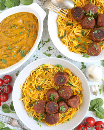 Spaghetti with thick orange sauce served with brown veggie balls in two white bowls. Leftover sauce is in the corner in a small bowl.