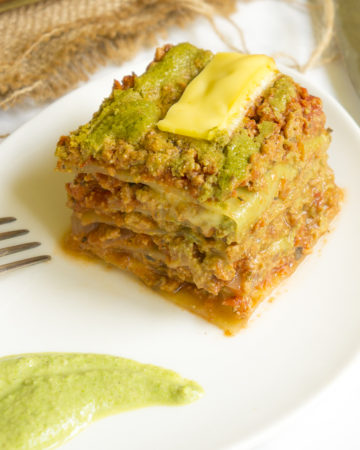 One portion of green red lasagna with cabbage leaves served on a white plate.