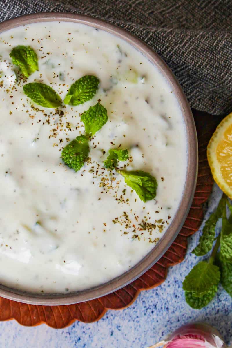 Cacik Turkish yogurt dip in a brown bowl served with mint and lemon.