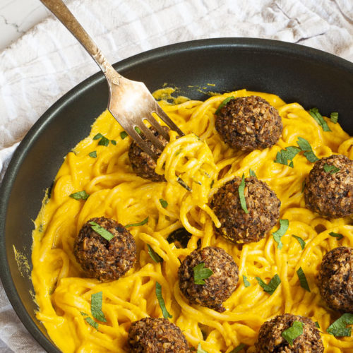 Yellow pasta sauce in a frying pan topped with mushroom meatballs.