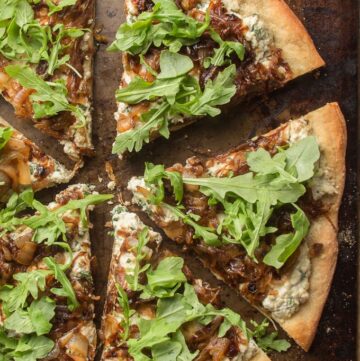 Pizza with cream cheese-like herby sauce, dark brown caramelized onion, and arugula.