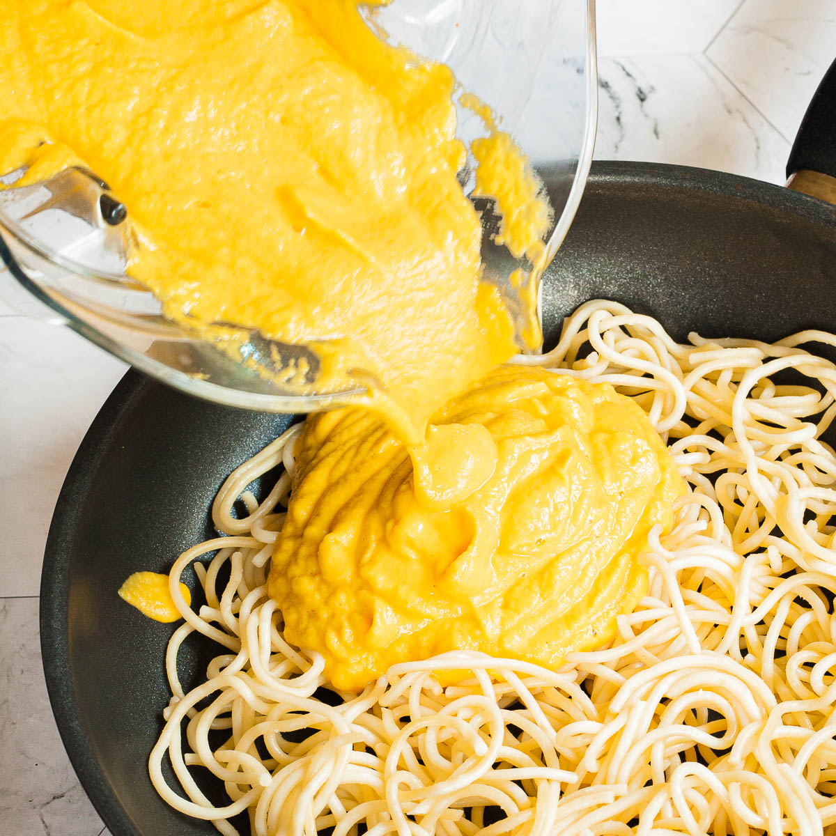 Yellow pasta sauce poured on top of spaghetti in a frying pan.