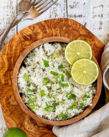 White rice with chopped cilantro and lime slices in a wooden bowl.