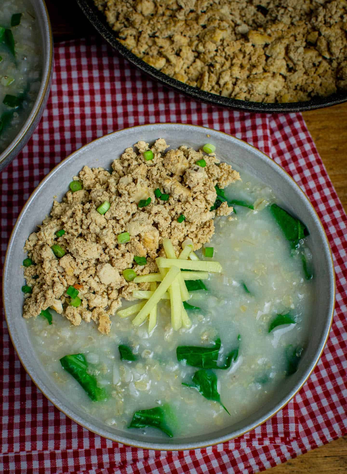 An opaque soup called congee with leafy greens and light brown crumbles