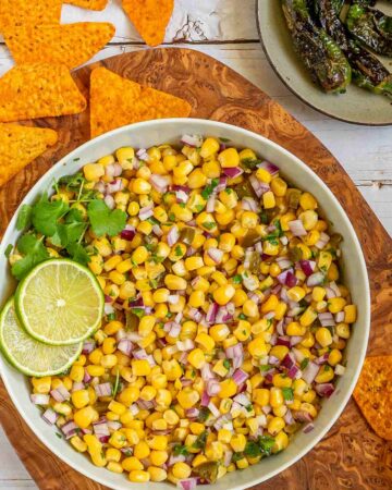 Corn salsa in a large white bowl with lime slices and nachos.