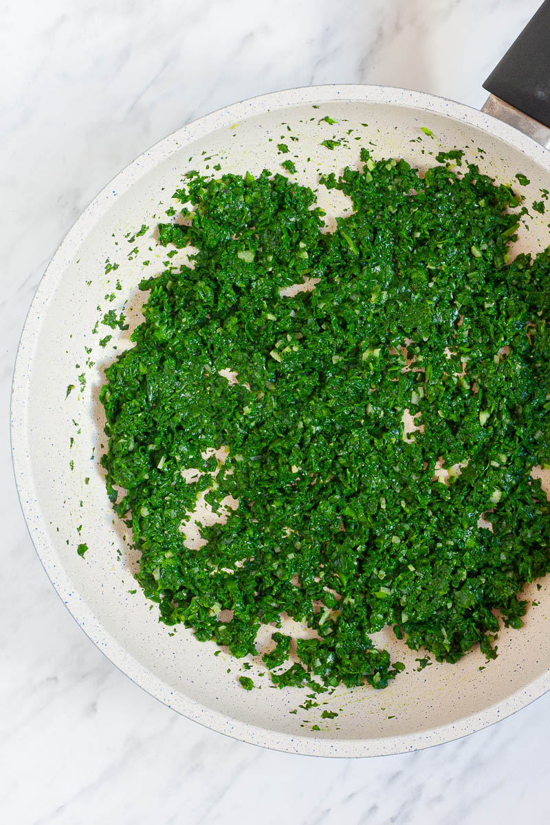 A white frying pan from above with chopped and cooked spinach