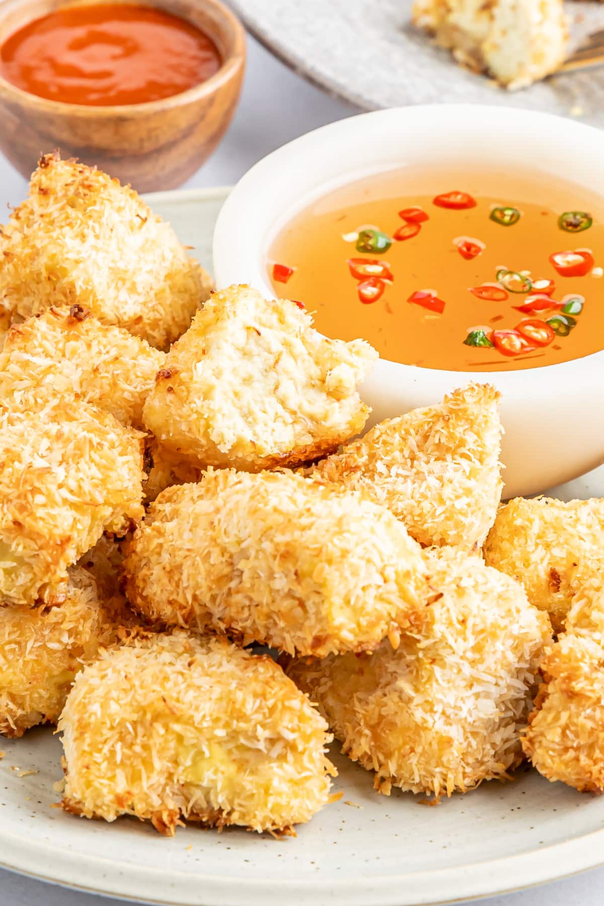 Side view of a rustic white plate of crispy breaded tofu with a smaller white bowl of dipping sauce.