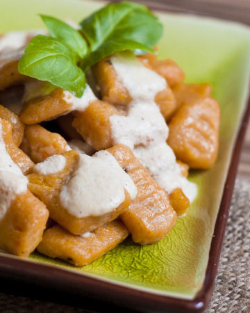 Orange rectangular-shaped pasta drizzled with white sauce on a green plate.