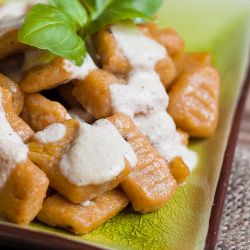 Orange rectangular-shaped pasta drizzled with white sauce on a green plate.