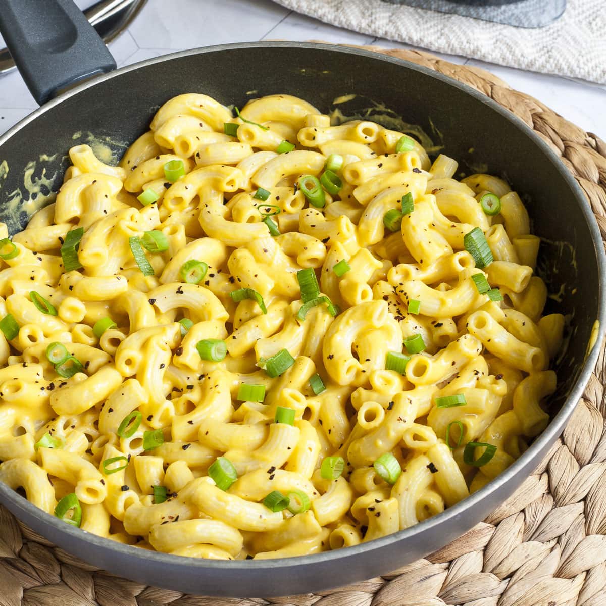 Small white bowl of fusilli pasta mixed with Easy Vegan Mac and Cheese No nuts Sauce and topped with eggplant and oyster mushroom garnish