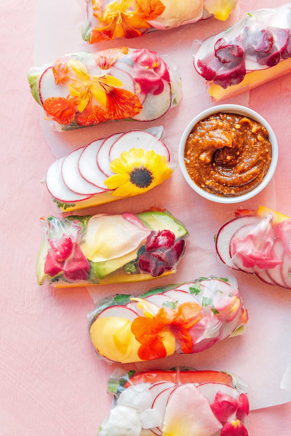 Colorful rice paper rolls with flowers on a pink surface