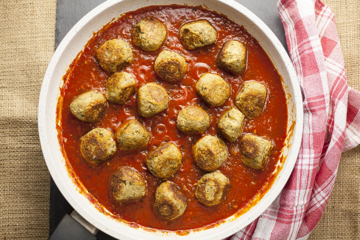 Overlay photo of a frying pan. Lot of small eggplant balls in marinara sauce