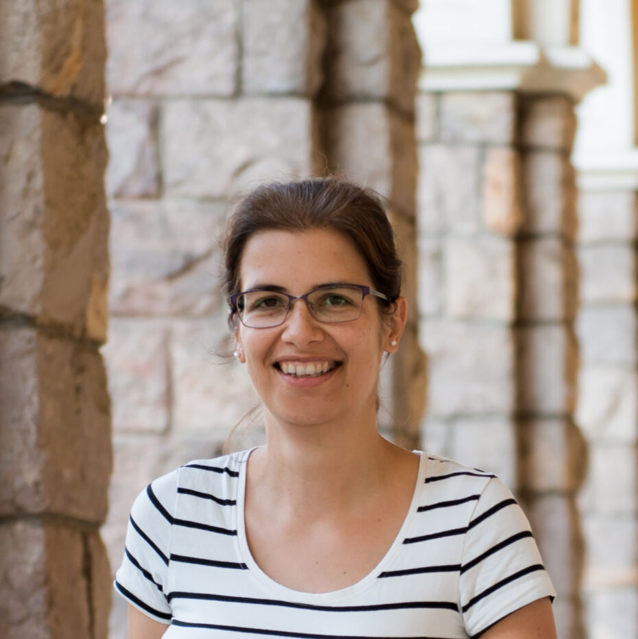 A woman with glasses and blue white stripe T-shirt in from of stone columns.