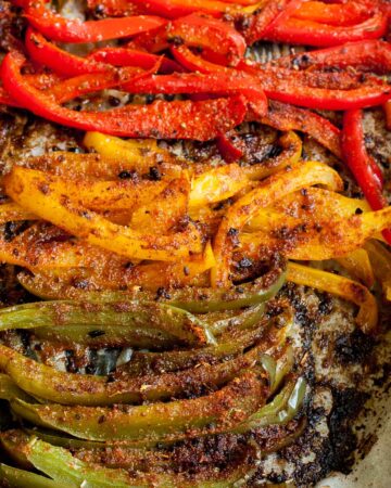 Close-up of roasted brown crispy seasoned red, yellow, green bell pepper strips after baking with tongs taking a couple of them.