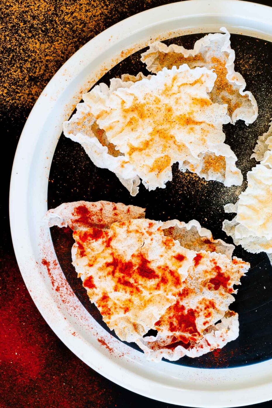 Several puffed rice paper sheets sprinkled with different spices red yellow and brownish on a black plate
