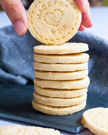 A stack of thin round cookies on a black board. A hand is holding the top cookie