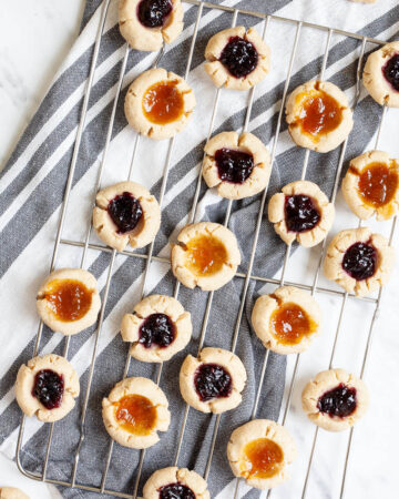 Several round cookies with orange and purple jam filling placed on a wire rack from above.