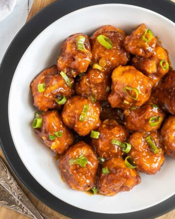 Orange sauce glazed cauliflower florets sprinkled with chopped green scallions in a white plate.