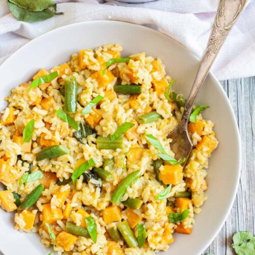 Two white bowls of fried rice in an orange sauce with sweet potato cubes and green bean pieces, A fork is placed inside the dish.
