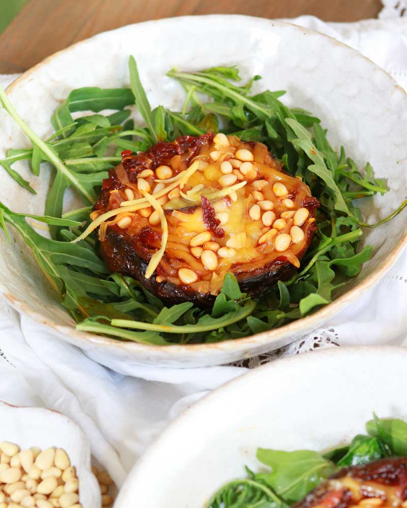 Large mushroom cap on a nest of arugula topped with melted cheese and pine nuts