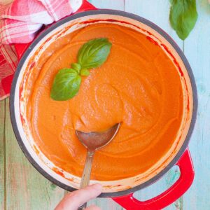 Red and white dutch oven with a smooth creamy light red sauce topped with basil leaves.
