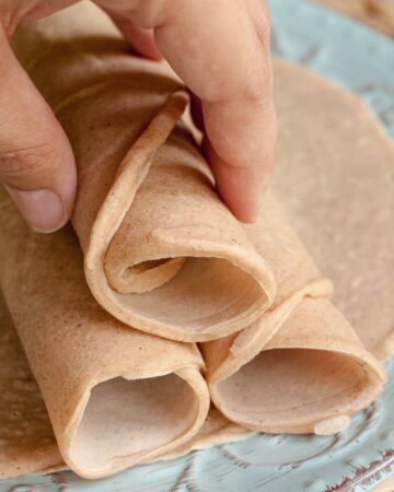 3 rolled tortillas on top of one flat placed on a light blue plate.A hand is holding the top one.