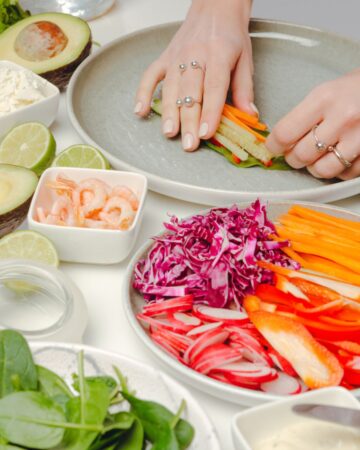A women is preparing spring rolls and placing a set of julienne vegetables on a plate.
