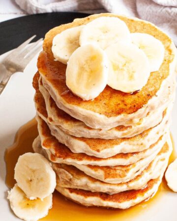 White plate with a stack of pancakes topped with banana slices
