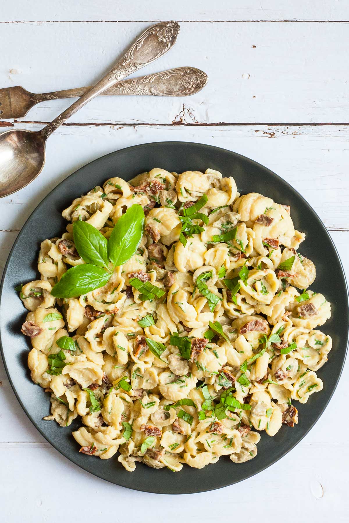 Black plate with shell pasta, sun-dried tomato pieces, and basil.