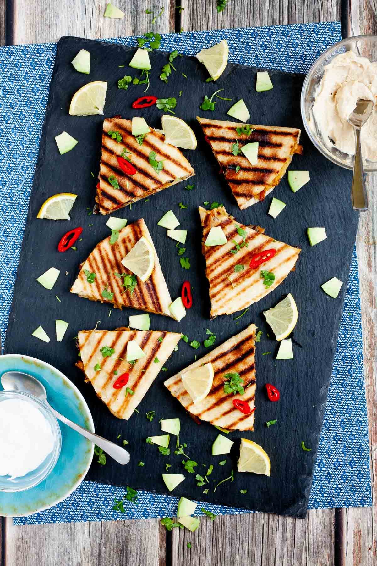 Several quesadilla triangles filled with black beans, red pepper, avocado slices sprinkled with fresh cilantro in a black board