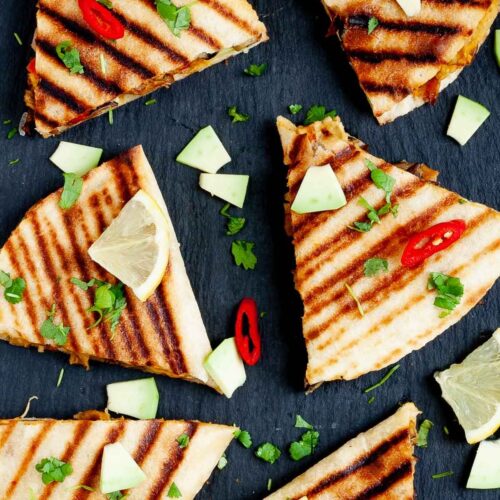 Several quesadilla triangles filled with black beans, red pepper, avocado slices sprinkled with fresh cilantro in a black board