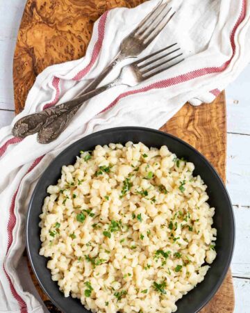 Black plate with small dumplings, in Hungarian nokedli sprinkled with freshly chopped green herbs.