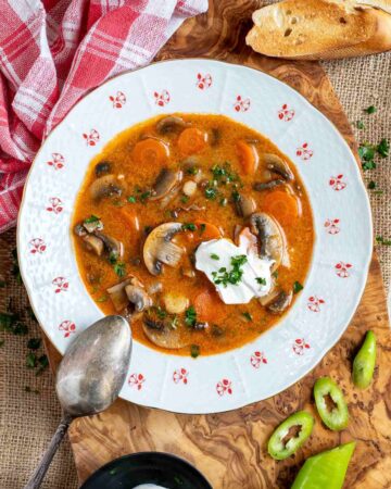 A bowl of Hungarian mushroom soup with sour cream on a wooden cutting board.