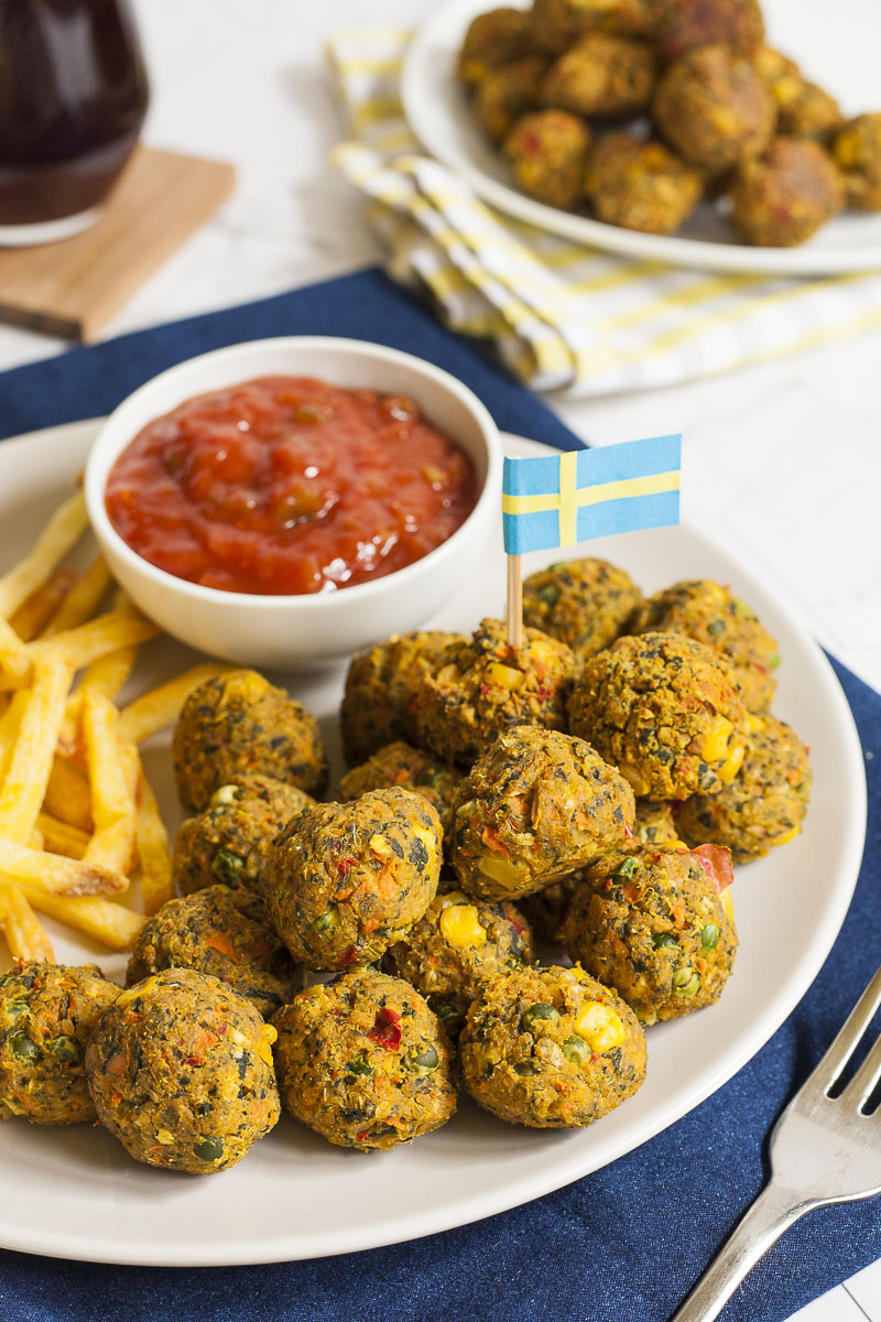 White plate full of small colourful balls with fried potato sticks and a small white bowl with red sauce. A blue yellow flag is stuck in one ball