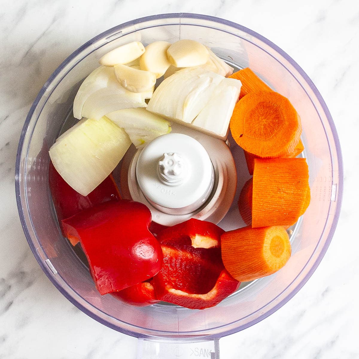 Food processor with roughly chopped carrots, onion, red pepper and garlic cloves