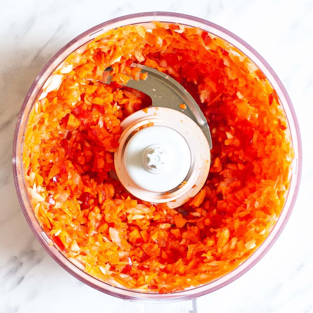 Food processor with red and orange veggie pieces.