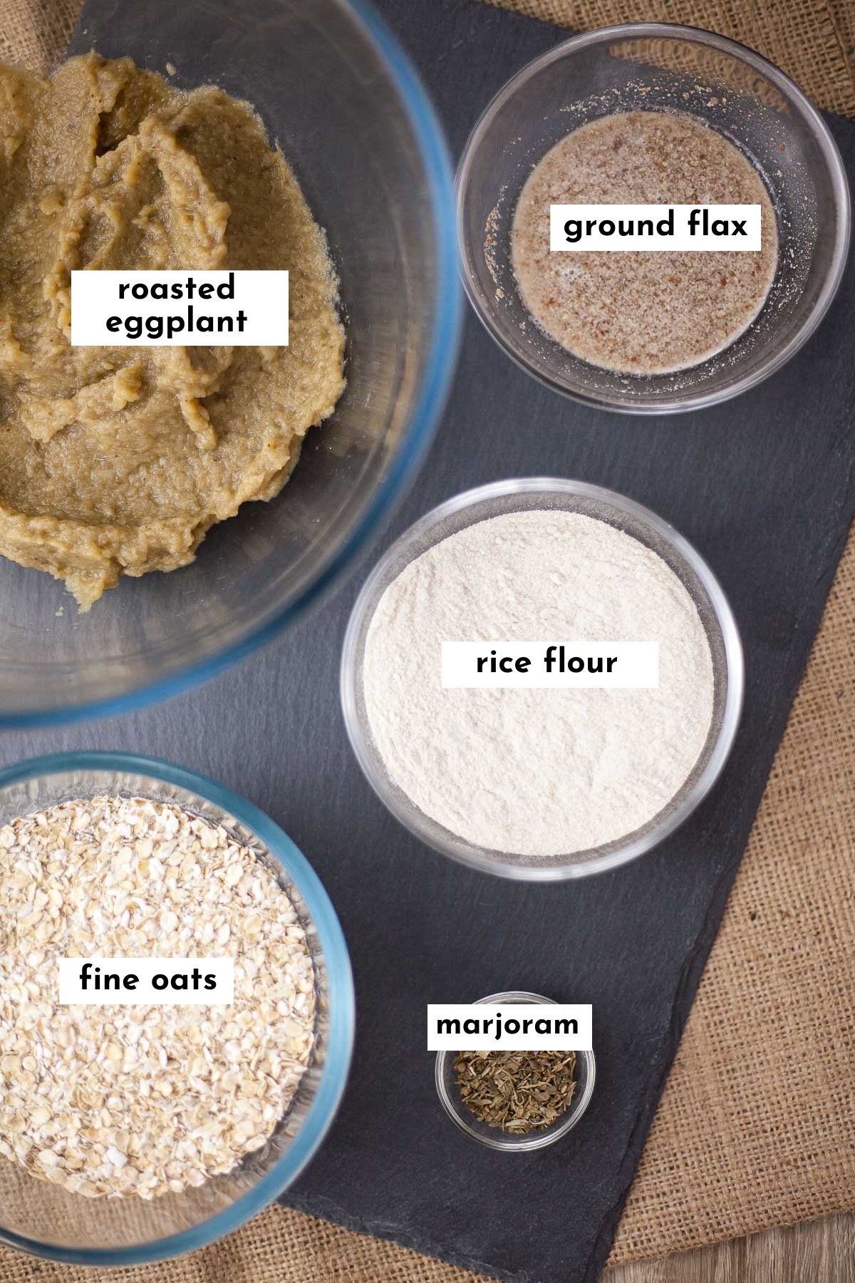 Ingredients of eggplant meatballs are measured in small glass bowls: brown pureed eggplant, oats, white flour, marjoram and flax seed in water