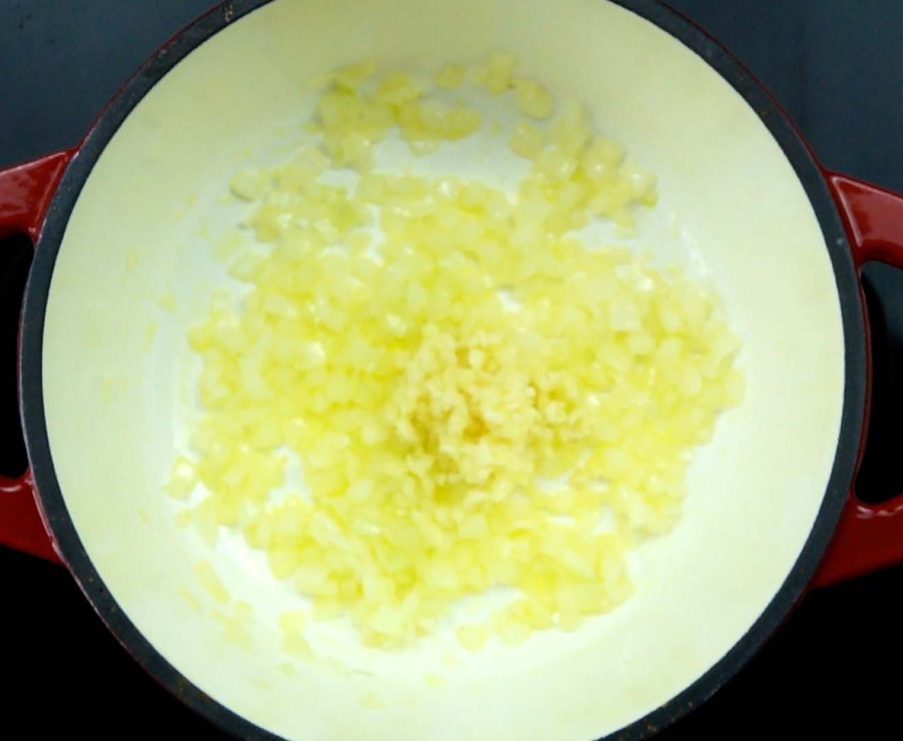 Red white Dutch oven with chopped onion and garlic.