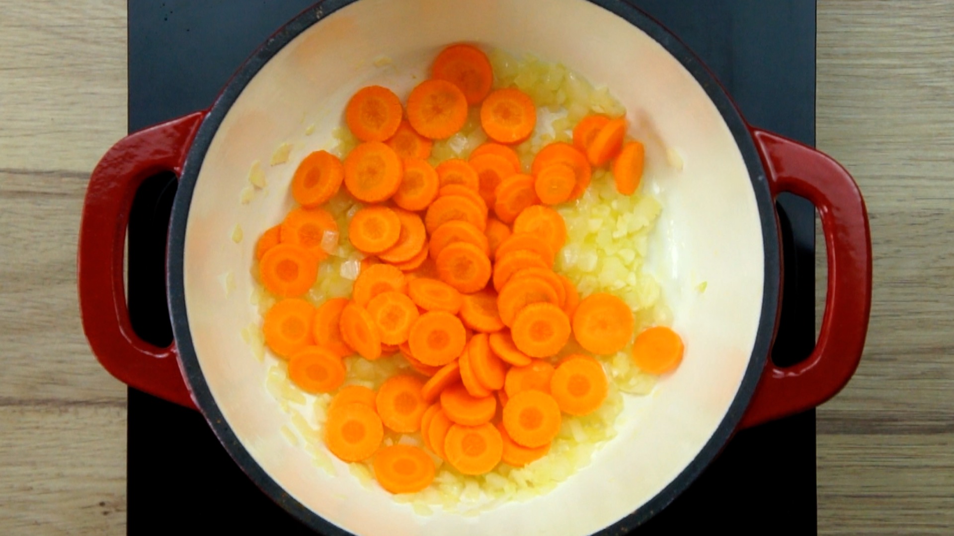 Red white Dutch oven with chopped onion, garlic and sliced carrots.