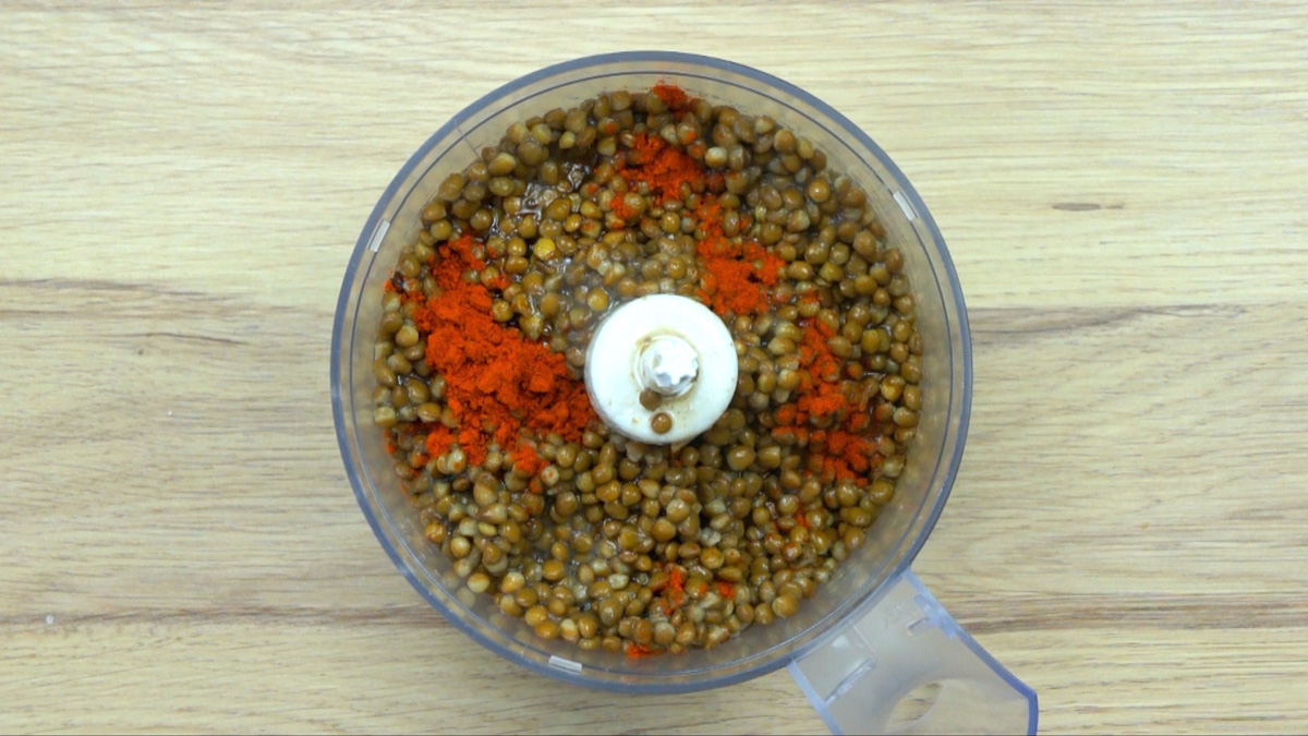 Food processor with lots of pre-cooked veggie pieces, lentils and small heaps of red powder.
