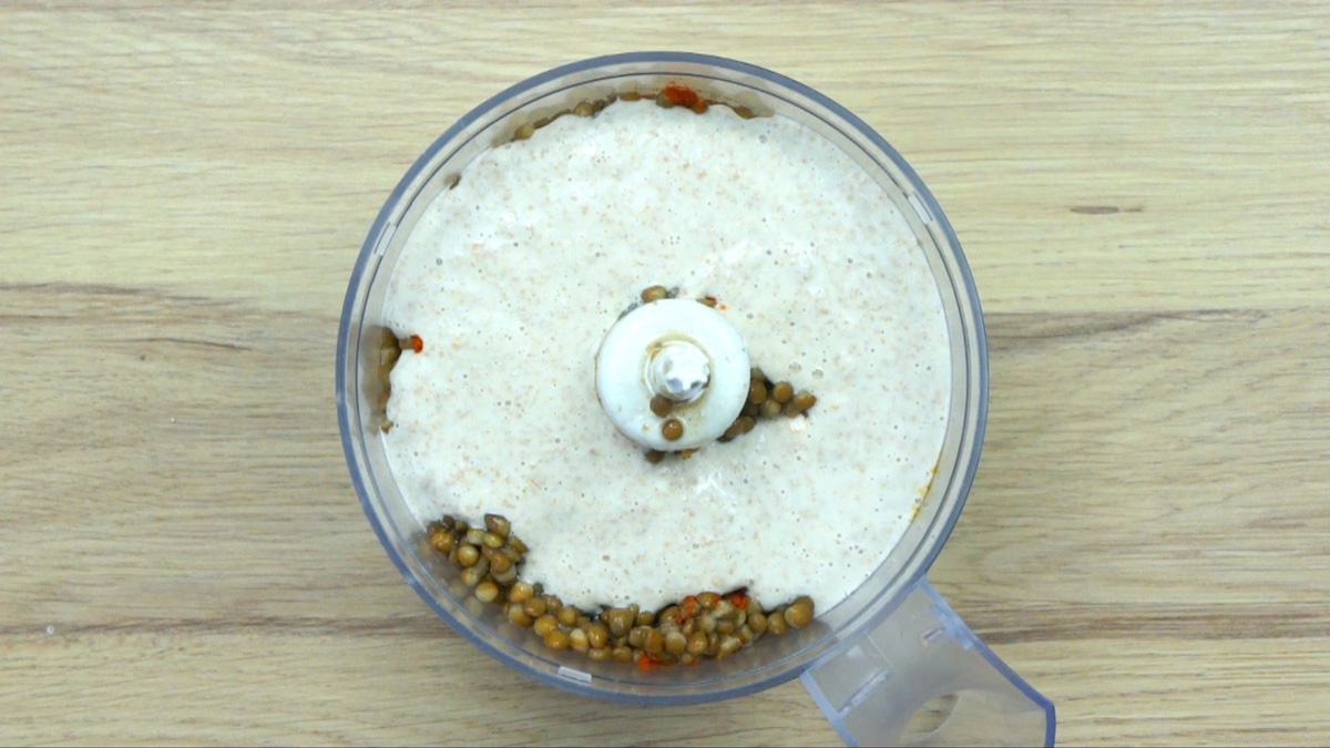 Food processor with lots of pre-cooked veggie pieces and white sauce on top.